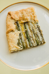 single serving, rectangular slice of an asparagus gruyere galette on golden yellow plate
