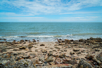 Breaking wave, sand, beach stones, see distant land across the bay. rocks, sea and blue sky