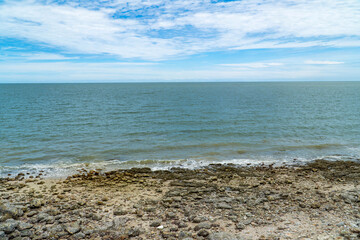 Breaking wave, sand, beach stones, see distant land across the bay. rocks, sea and blue sky