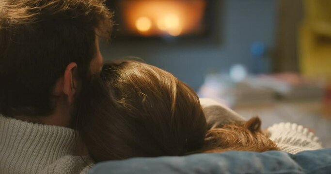 A happy young couple hugging and cuddling on the couch in front of a fireplace