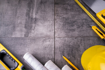 Contractor theme. Tool kit of the contractor: yellow hardhat, libella, hand saw. Plans and notebook on the gray tiles.