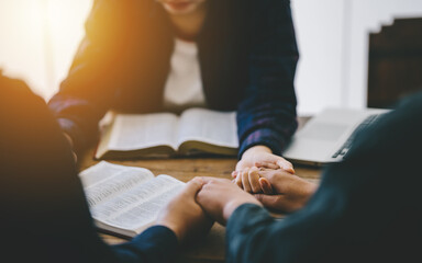 Christian group of people holding hands praying worship to believe and Bible on a wooden table for devotional for prayer meeting concept.