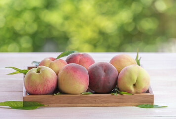Fresh Sweet Peach on green bokeh background, Pink and yellow Peach fruit with leaf on wooden plate.