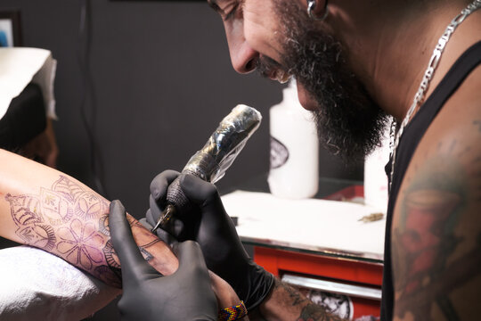 Joven artista de tatuajes barbudos realiza un tatuaje en el brazo de un cliente