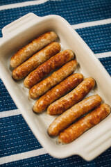 browned, cooked individual breakfast sausage links in white dish on blue and white stripe cloth