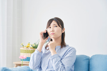 リビングでスマホで電話しながら考える女性