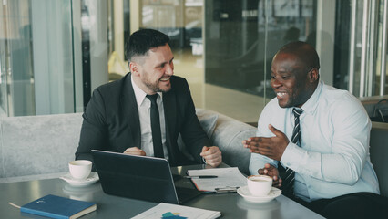 Two businessmen talking ang laughing in modern cafe. Men having fun and joking looking at laptop...