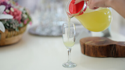 Woman hand pours juice or lemonade from jug into glass