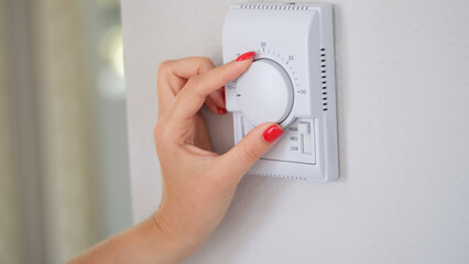 Woman's hand regulating the temperature of central heating of house on thermostat