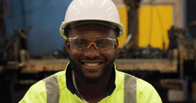 POV Portrait of professional industrial engineer African man wearing helmet and goggles looking at camera with a smile in manufacturing industry. 4.0 Smart Factory. Technology or Innovation concept.