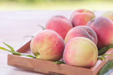 Fresh Sweet Peach on green bokeh background, Pink and yellow Peach fruit with leaf on wooden plate.