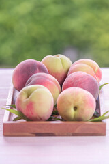 Fresh Sweet Peach on green bokeh background, Pink and yellow Peach fruit with leaf on wooden plate.