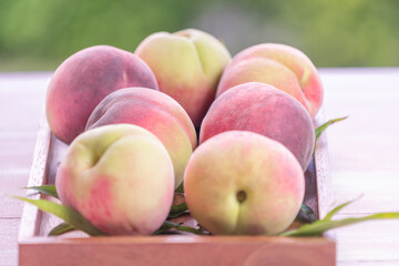 Fresh Sweet Peach on green bokeh background, Pink and yellow Peach fruit with leaf on wooden plate.