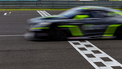 Race car blurred motion crossing the finish line on international circuit speed track, Motion blur Racing car crossing finish line on asphalt main straight racetrack. - obrazy, fototapety, plakaty