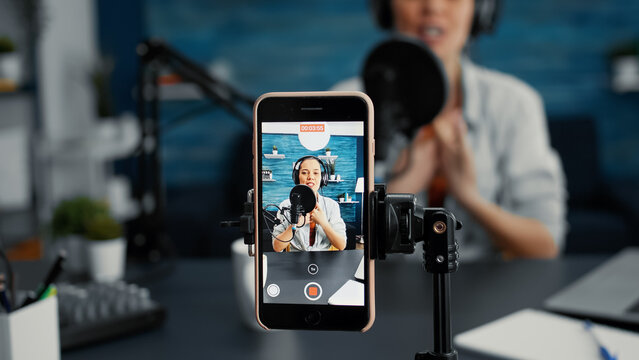 Modern smartphone recording vlogger talking to public while sitting at home studio desk. Famous influencer filming podcast show with touchscreen display device while sitting in living room. Close up