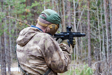 a man in camouflage shoots from a machine gun in the forest