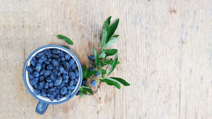 Blue honeysuckle in metal mug on wood background. Fresh honeysuckle berries harvest from berry farm.