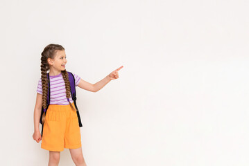 A child with a satchel points with his index finger at your advertisement on a white isolated background. Preparatory summer courses for children. Copy space.