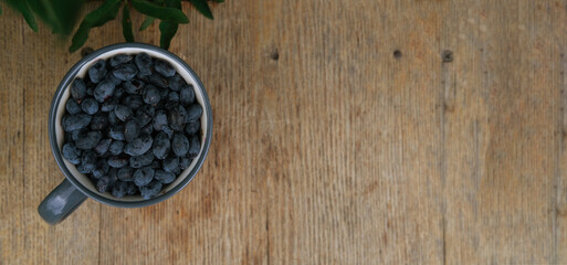 Blue honeysuckle in metal mug on wood background. Fresh honeysuckle berries harvest from berry farm.