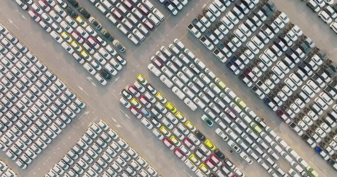 Aerial view of large parking new cars distribution center of modern seaport. Lot of vehicles waiting for sale and transportation shipping by freight cargo vessel ship. Automobile industry.