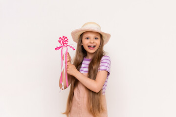 A little girl holds a caramel lollipop on a stick in. Baby in a sundress and a summer straw hat on a white isolated background.