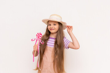 A little girl holds a caramel lollipop on a stick in. Baby in a sundress and a summer straw hat on a white isolated background.