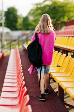 A teenage girl with a backpack walks through the stands of the school stadium. Rear view