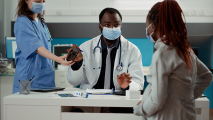 General practitioner giving bottle of pills as prescription treatment to woman expecting child in medical office. Male obstetrician attending appointment with pregnant person to give medication.