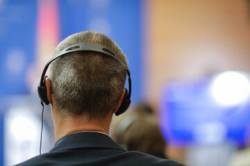 Shallow depth of field (selective focus) details with a caucasian man wearing translation headset during an international event.