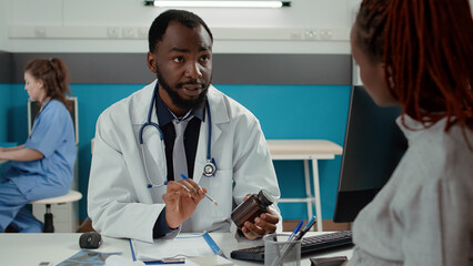 Male obstetrician giving prescription pills in bottle to future mother with baby bump, meeting in...