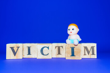 text the word victim from wooden letters,on the letter sits a miniature toy newborn.Purple,veri peri background,copy space.