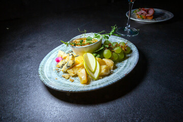 Delicious cheese platter - slices of several types of hard and soft cheese, served on a plate with ripe grapes, an apple and a sprig of peas