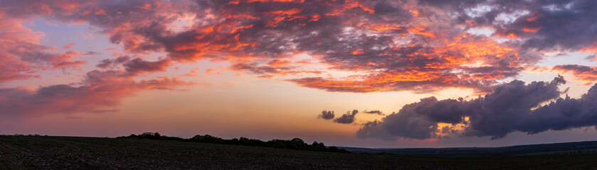 Sun sitting on the horizon against the background of colorful clouds in the sky 