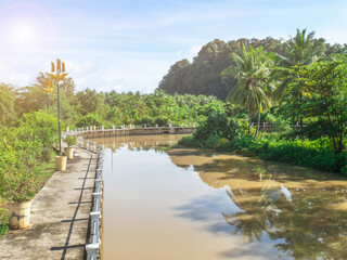 Fototapeta premium View of the walkway through the canal that is a park, see green trees and mountains. There is a reflection of the trees in the river.