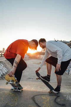 Shot Of Two Tattooed Hipster Boys Skateboarding At Skate Park At Sunset.