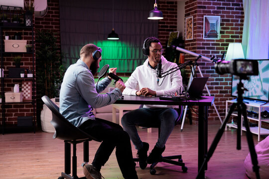 Multiethnic team of people broadcasting internet podcast, recording video discussion on camera. Influencer and guest talking on online livestream to create social media channel content.