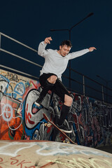 Portrait of hipster boy showing tricks on skateboard at skatepark with graffiti walls.