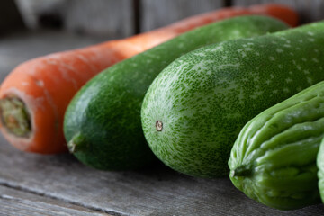 Vegetable shot showing line up of carrot, hairy melon and bitter gourd on wooden platform.