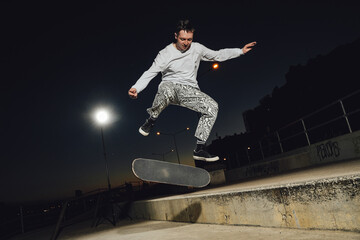 Portrait of cool dude doing stunts on skateboard at night at skateboard there are no people.