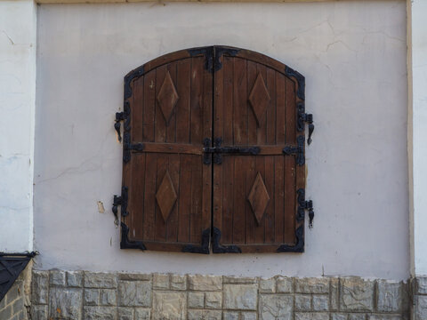 Closed wooden shutters decorated with rhombus on a white wall. Brown window with closed lids on the stone wall.