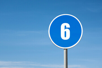 '6 (six)' sign in blue round frame. Blue sky is on background