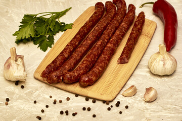 spicy smoked sausages on a cutting board next to red pepper garlic spices and herbs on the table
