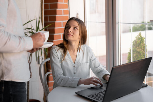 Image of smiling woman 20s working on laptop and man with coffee for wife, together while sitting at home