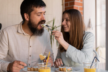 Young couple eating meal at home, loving woman feeding her boyfriend. Lovers having tasty helthy breakfast in kitchen, enjoying spending morning time together, close up