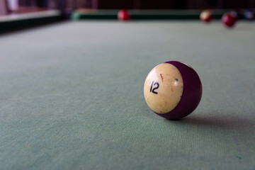 An old billiard ball with the number 12 in lilac lies on the faded cloth of the billiard table