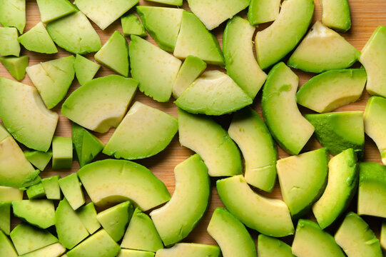 Vegetarian background cut into small pieces of avocado on a wooden cutting board. top view