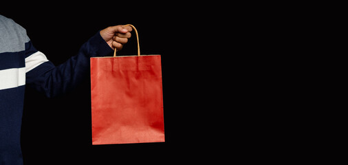Hand holding a red paper bag with a handle on a black background