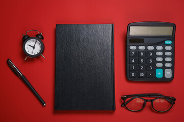 Male black notepad ballpoint pen and calculator, small alarm clock and glasses on dark red...