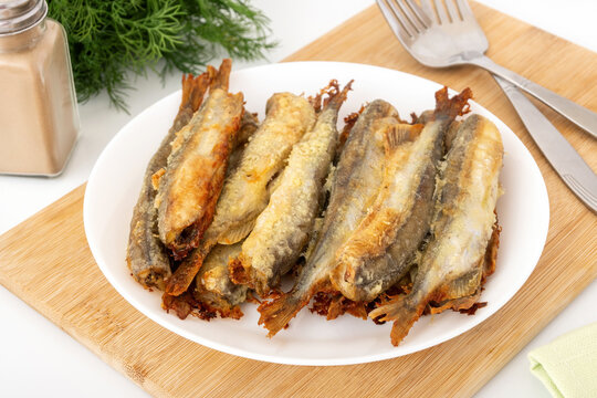 Baked capelin with crispy crust on cutting board. Small fat fish for cheap and healthy diet.