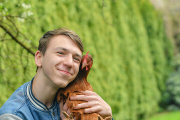 The boy holds a chicken in his hands and hugs her.